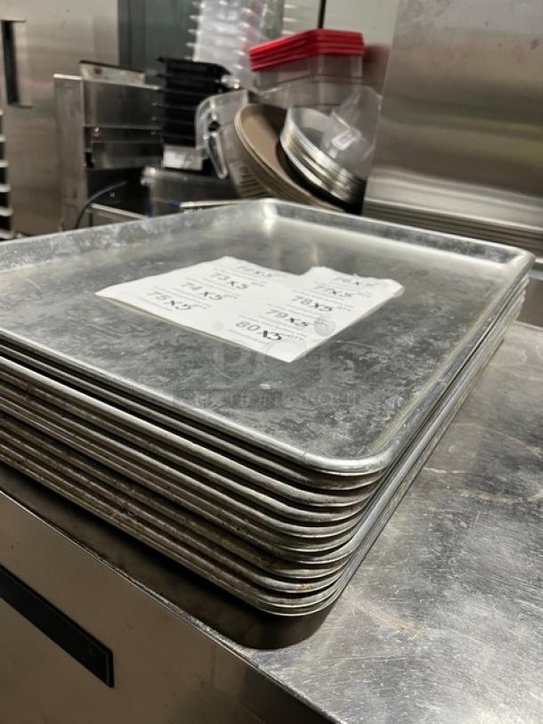 Commercial stainless steel full-size sheet pans stack, durable, used condition. Includes pricing labels on top pan.