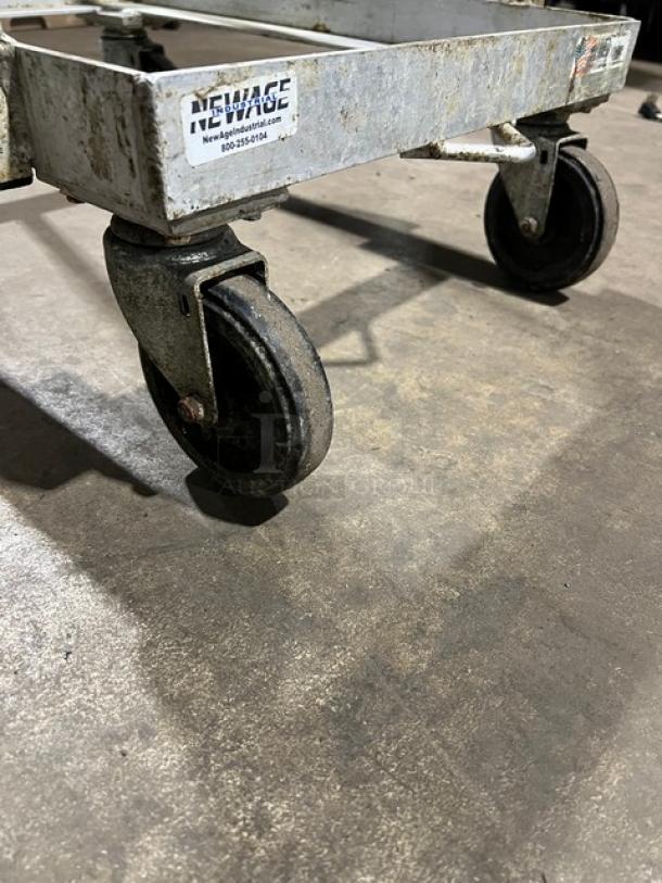 New Age Industries heavy-duty sheet pan dolly on casters, metal frame, visible wear, logo label with contact info.