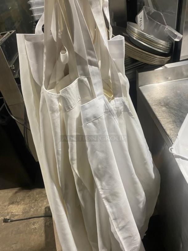 White full-length bib-style aprons hanging, commercial quality, excellent condition. Ideal for restaurant or catering use.