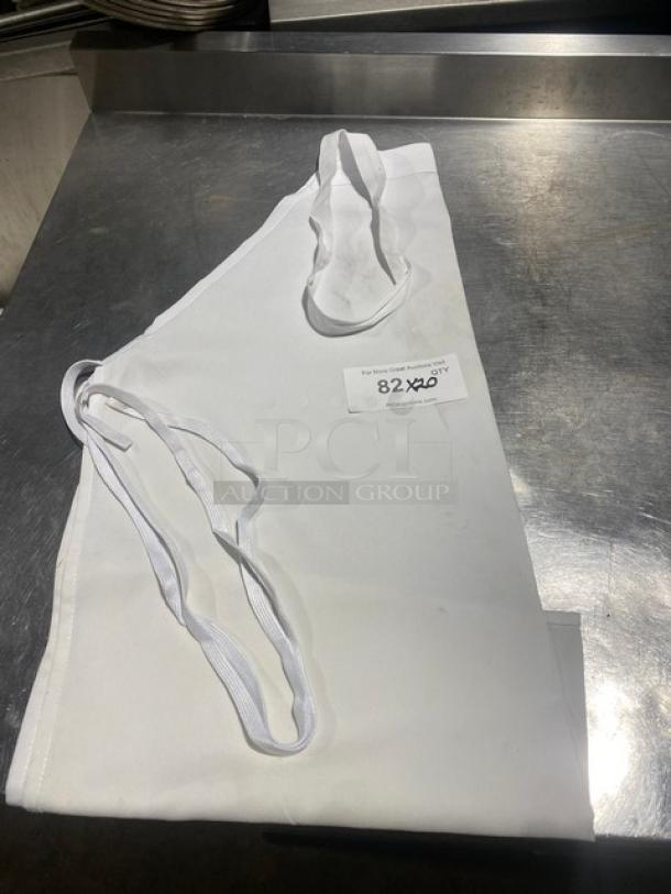 White full-length bib apron, commercial style, neatly folded. Includes tag indicating "82X20" quantity.