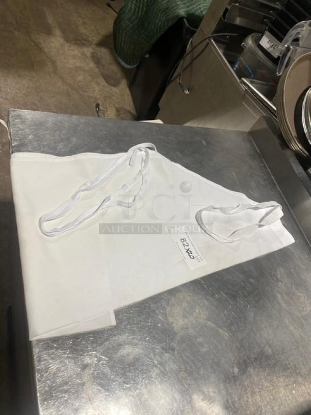 White full-length bib style apron, commercial grade, neatly folded on a metal surface. Tag shows "82.40 X". Excellent condition.