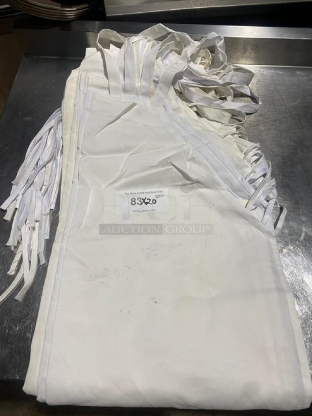 Commercial white full-length bib aprons, bundled with straps. Slight signs of use. Label reads "83X20 QTY."