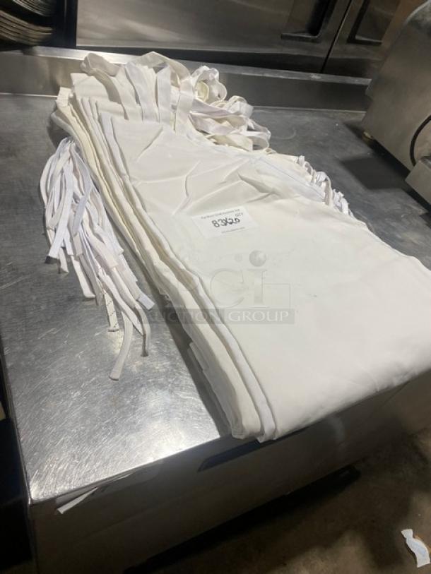 Commercial white full-length bib style apron in good condition, neatly stacked with multiple pieces, featuring a visible label.
