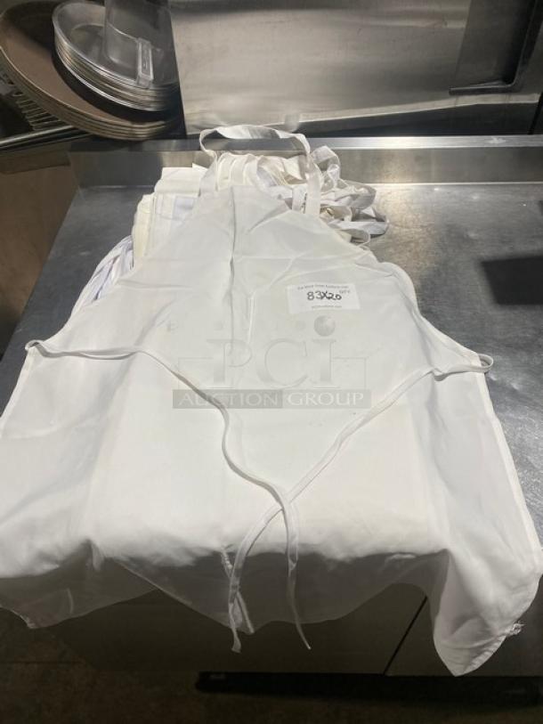 Commercial white full-length bib apron, 20X your bid, pile displayed. Features straps, clean condition, label visible.