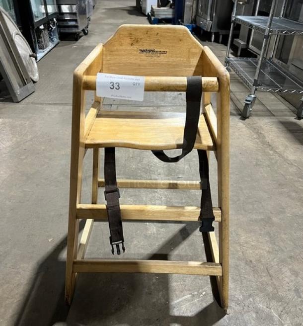 Commercial wooden highchair with safety strap, in good condition. Features sturdy construction and visible warning labels.