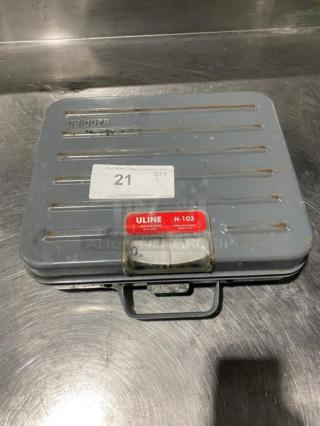 Rubbermaid Peluoze 100 lb analog shipping scale, model FG4100UD, in briefcase style. Visible wear and labels present.