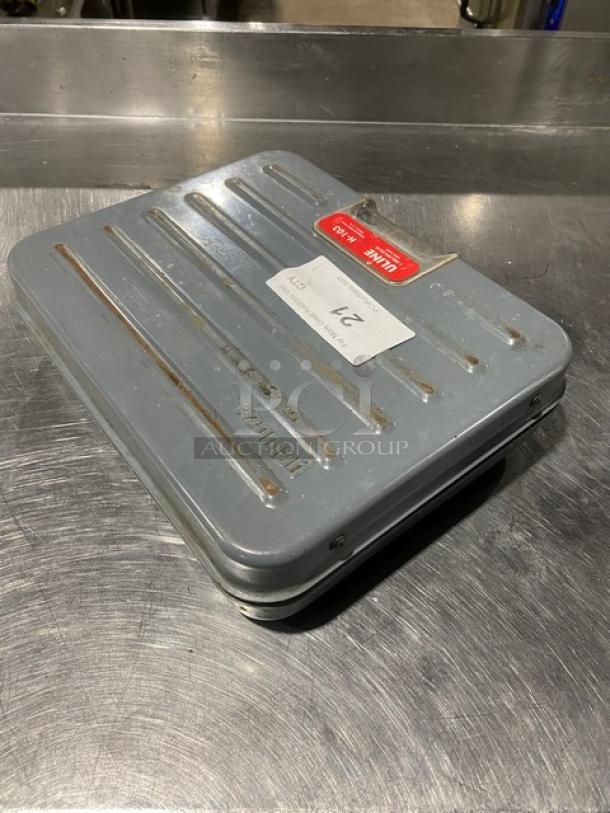 Rubbermaid Peluoze FG4100UD 100 lb analog shipping scale, briefcase-style, metal casing, visible wear, serial number 022672.