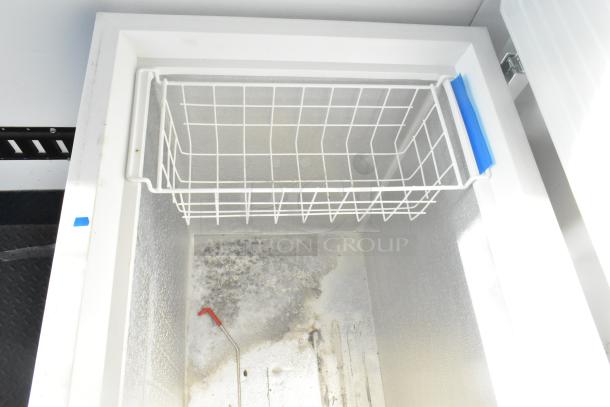 Interior of a Kenmore chest freezer inside a Southern Dimensions mobile kitchen trailer, showing a wire basket and insulated walls.