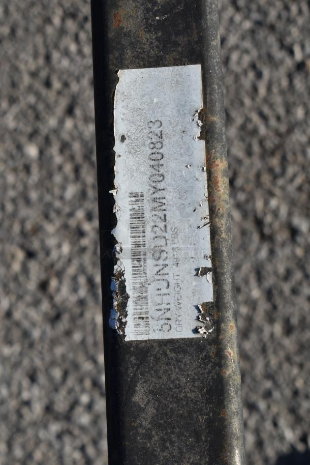 Close-up of a trailer tag with wear, displaying a serial number and weight information. Partially legible due to surface damage.