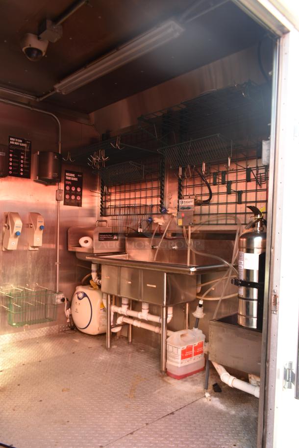 Interior of a 2020 ATX 28' retail trailer, featuring a stainless sink, fire extinguisher, pipes, and labeled hygiene instructions.
