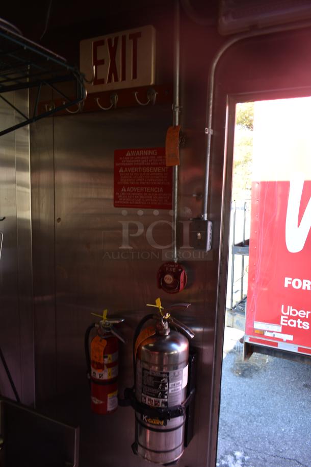 Inside view of ATX 28' cold food trailer showing exit sign, fire extinguishers, and warning signs for safety compliance.