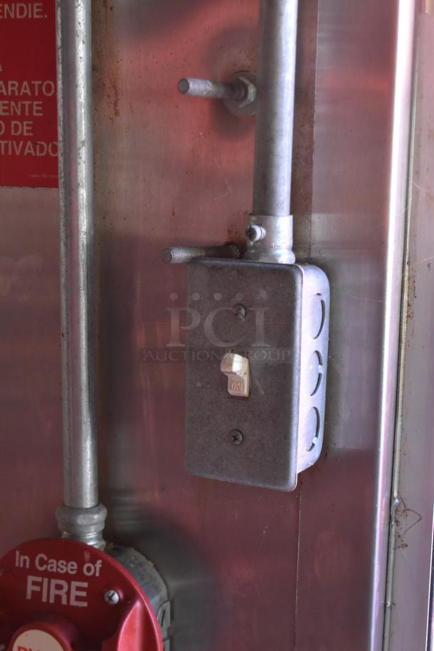 Metal toggle switch box with "On" label in a trailer kitchen. Features visible fire safety signage.