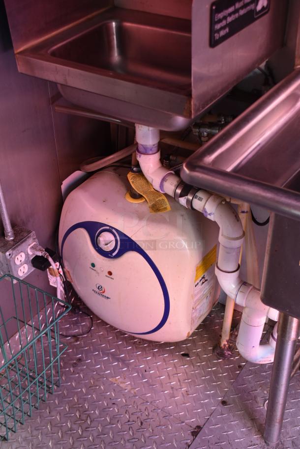 Interior view of ATX 28' trailer showing plumbing under a stainless steel sink, featuring a modern water heater and outlets.
