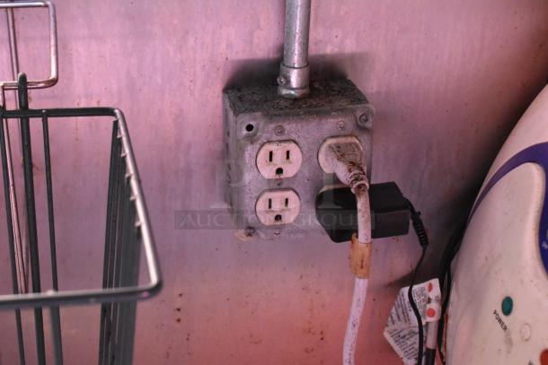 Electrical outlet in ATX 28' food trailer, showing plugged-in cords and part of surrounding equipment.