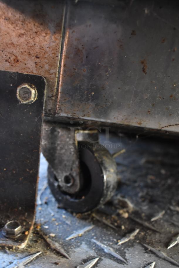 Close-up of a caster wheel on the ATX 28' cold food trailer. Dirty and rusted metal, showcasing wear and use.