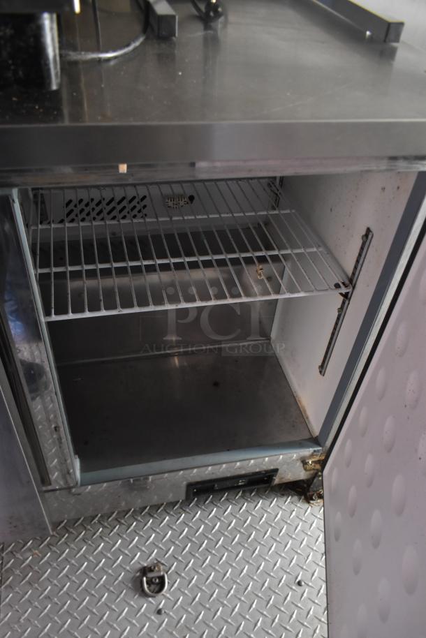 ATX 28' food trailer interior; open Arctic Air cooler with wire shelves, stainless steel counter, diamond plate flooring.