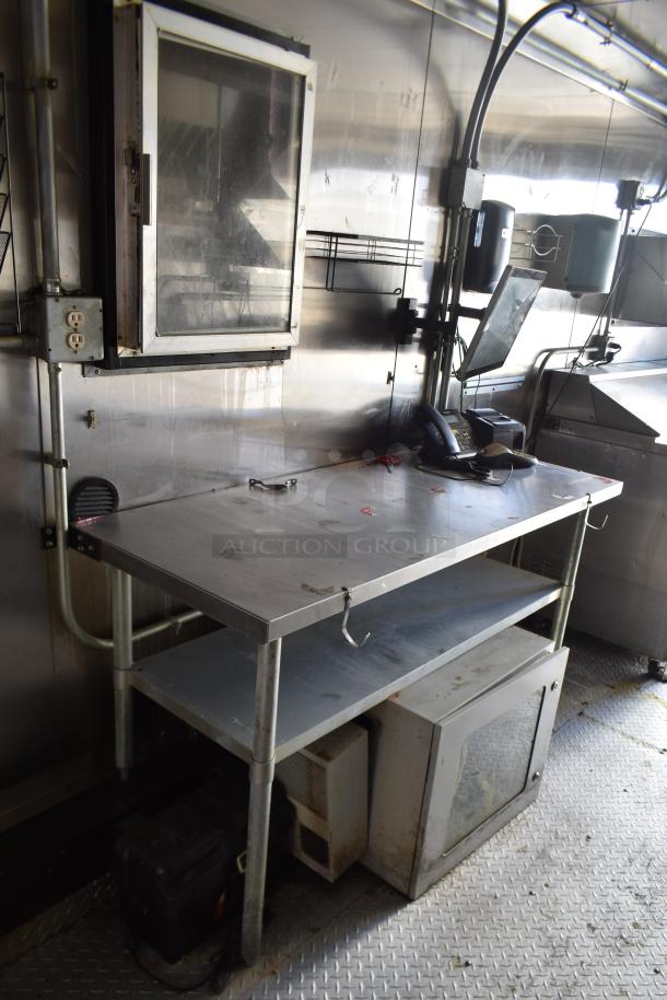 Interior of ATX 28' food trailer with stainless steel prep table, ventilation hood, shelving, and commercial phone setup.