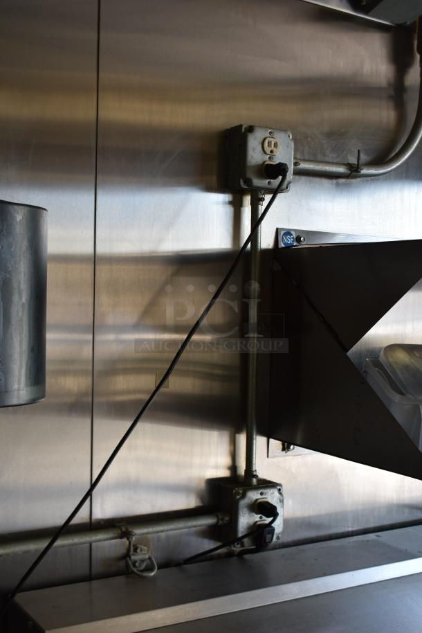 Interior view of a stainless steel commercial kitchen with outlets and NSF sticker, inside a 28' ATX food trailer.