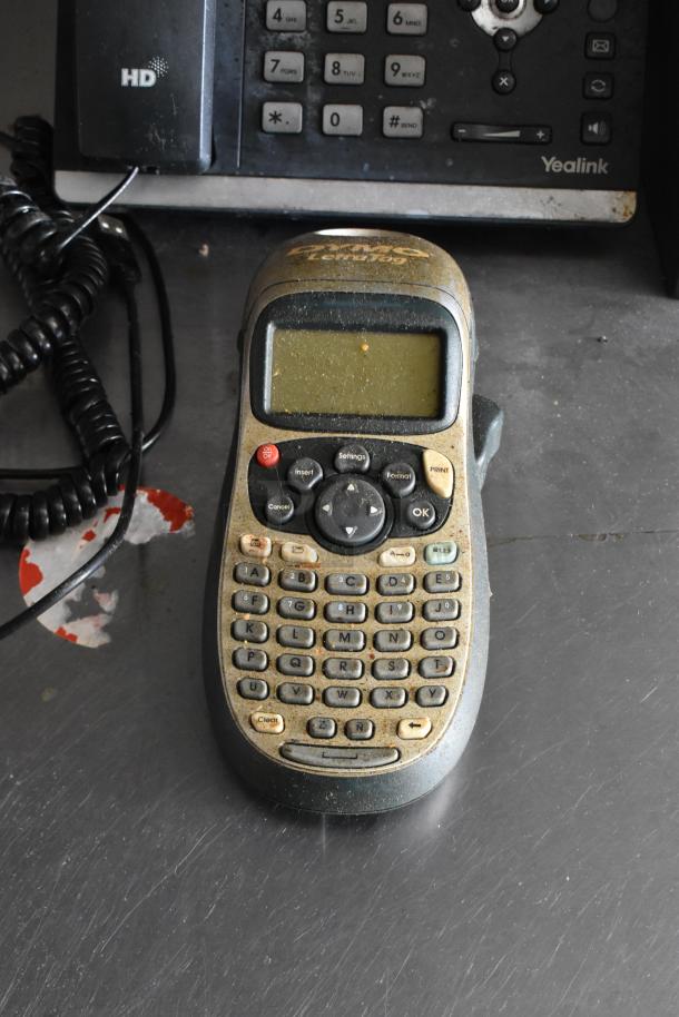 Dusty label maker with buttons, on a table next to a phone.