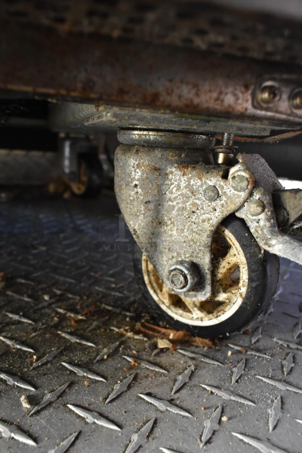 Close-up of a caster wheel on rusted metal flooring under the ATX 28' food and beverage trailer.