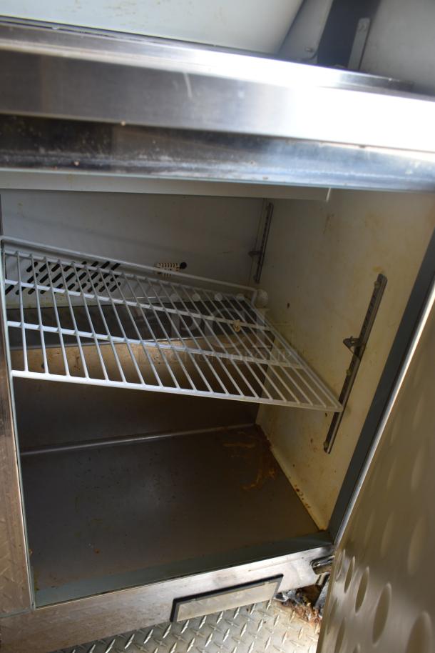 Interior of ATX 28' unbranded trailer with a commercial-grade refrigerator. Features metal shelves and clean surfaces.