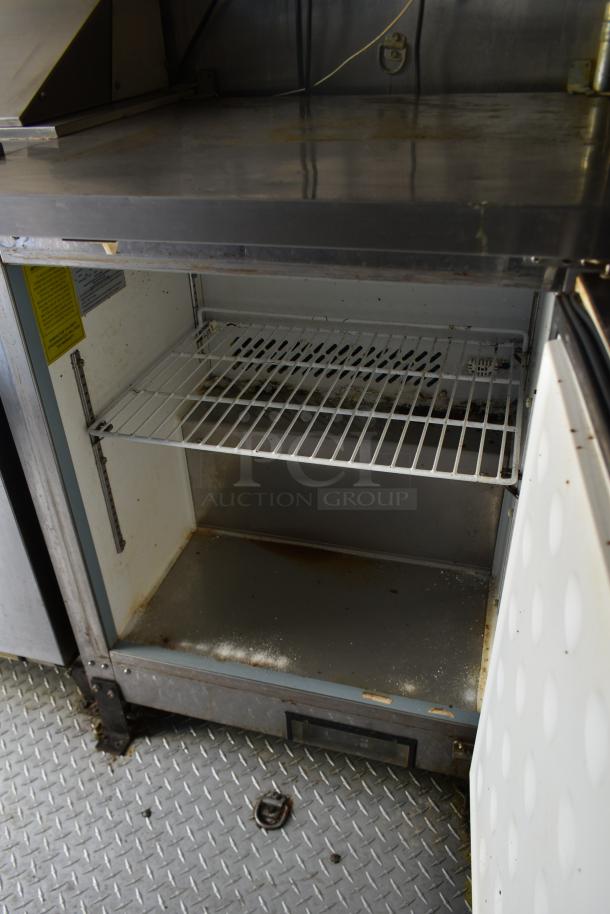 ATX trailer interior, showing stainless steel prep surface and open commercial cooler with shelves, minor wear visible.