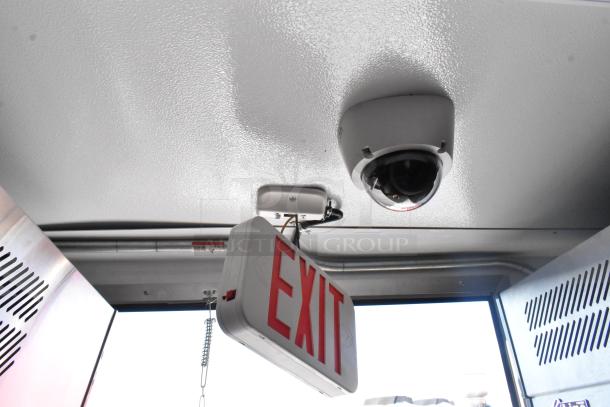 Interior view of a cold food and beverage trailer featuring a ceiling-mounted security camera and an illuminated exit sign.