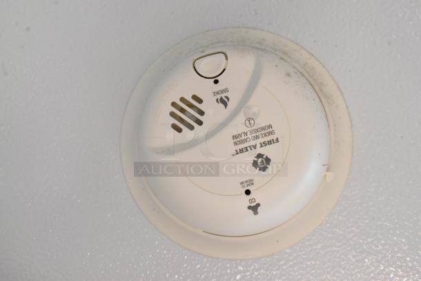 Smoke and carbon monoxide alarm mounted on the ceiling. White casing, labeled as First Alert, with test button and vents.