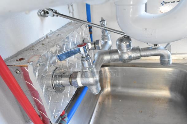 Stainless steel sink with dual faucets inside a fully equipped cold food and beverage retail trailer, featuring commercial-grade fixtures.