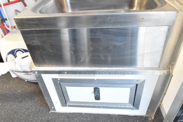 Stainless steel sink unit in a food trailer, featuring a lower storage compartment and commercial-grade fixtures.