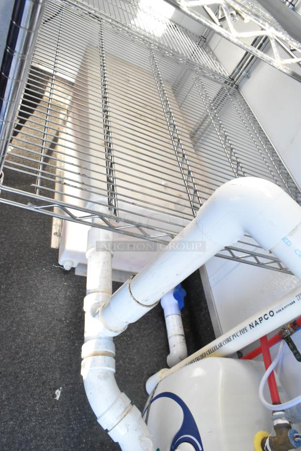 Interior of unbranded cold food trailer showing metal shelving and plumbing with NAPCO PVC pipes; commercial setup.