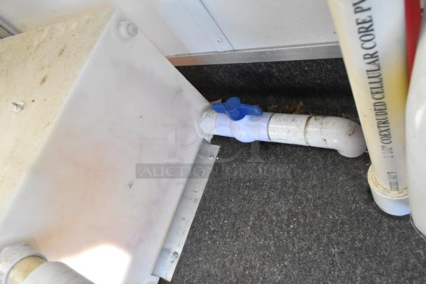Interior detail of unbranded cold food trailer showing a plastic pipe with a blue valve on a textured floor.