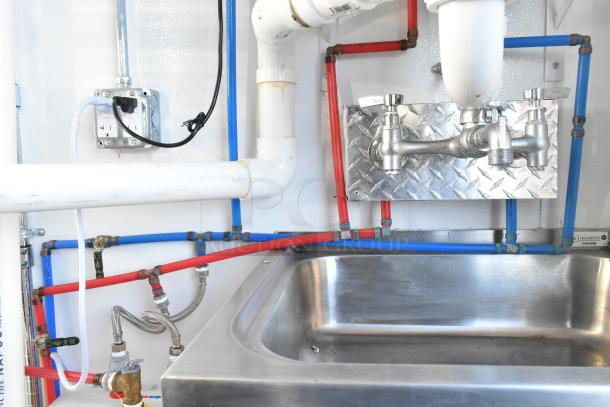 Unbranded cold food trailer sink area with plumbing. Stainless steel fixtures and PVC pipes visible.