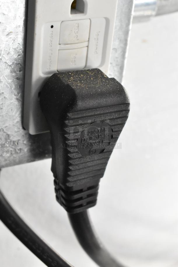 Close-up of a black power plug connected to a white electrical outlet inside a fully outfitted culinary trailer.