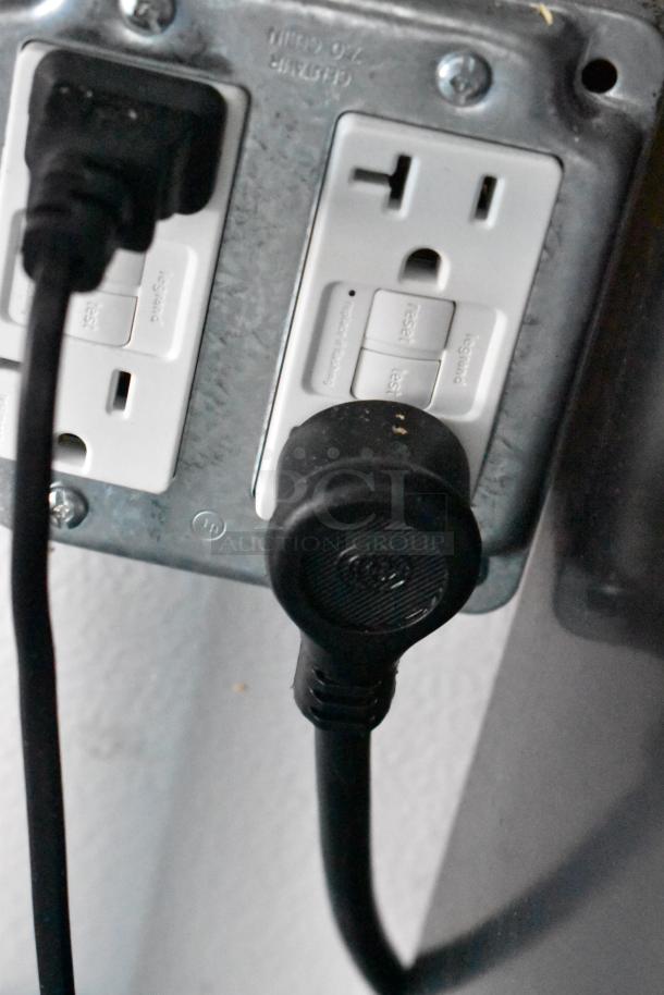 Electrical outlet with black power cords plugged in, mounted on a metallic plate.