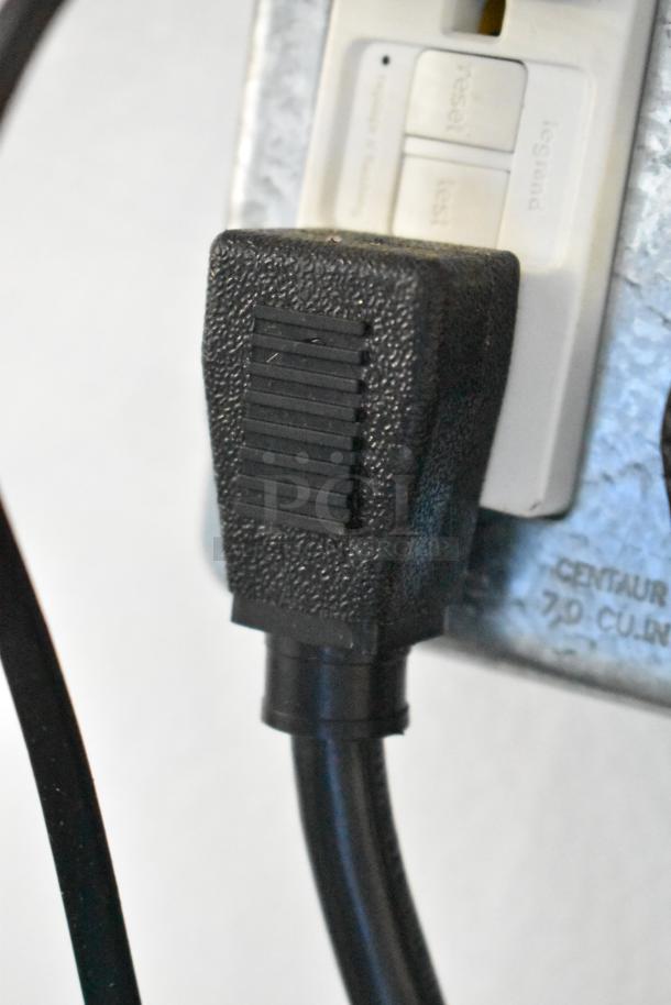 Close-up of a black power plug connected to a wall outlet. The outlet has reset and test buttons.