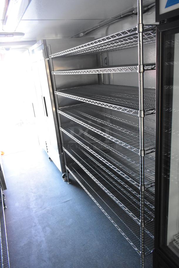 Unbranded cold food trailer interior with metal shelving. Includes True freezer, cooler merchandisers, and Turbo Air coolers.