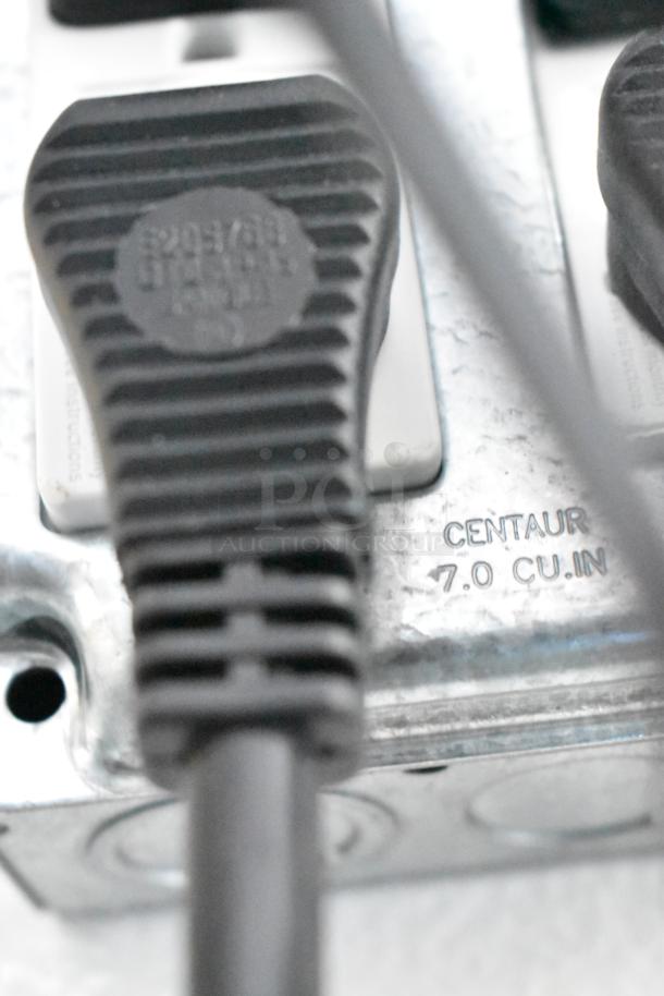 Close-up of a power cord plug in an outlet with a "Centaur 7.0 cu. in." marking on the metal plate.