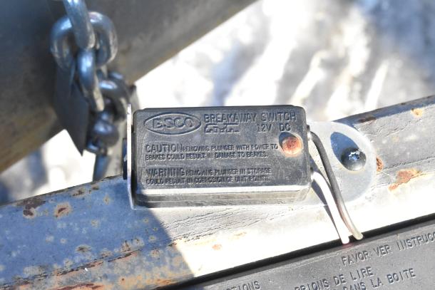 ESCO breakaway switch on Titanium Cargo trailer, 12V DC. Caution for brake damage and corrosion warning on metal surface.