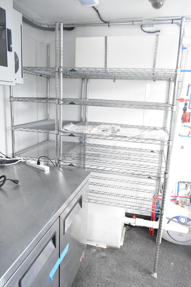 Unbranded cold food trailer interior with metal shelving, stainless steel counter, and plumbing fixtures, ready for use.