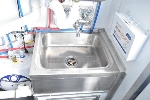 Stainless steel sink with plumbing in a cold food and beverage trailer. Includes Contractor's First Aid Kit mounted on the wall.