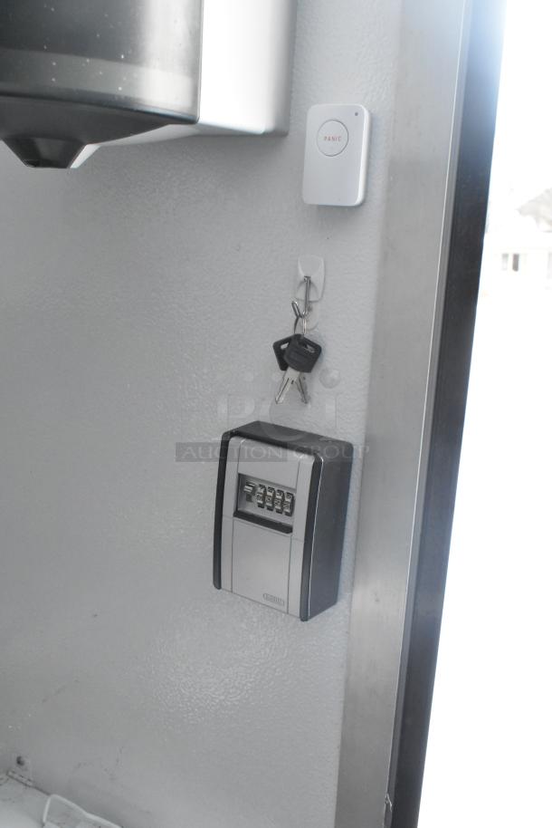Interior view of a fully outfitted retail trailer showing a keypad lockbox, keys on a wall hook, and a panic button.