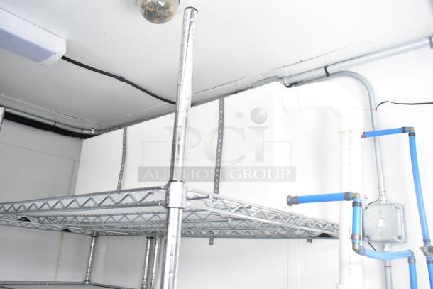 Interior view of a fully outfitted cold food trailer showing metal shelving and plumbing fixtures in excellent condition.