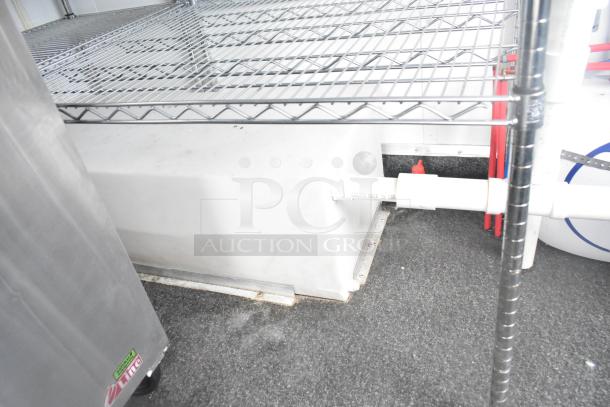 Interior view of a fully outfitted retail trailer, featuring metal shelving and a white tank with visible piping.