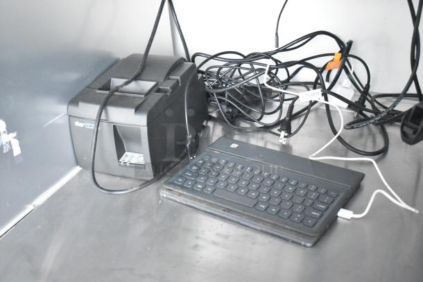 Printer and keyboard with tangled cords on a metal countertop in a food and beverage trailer.