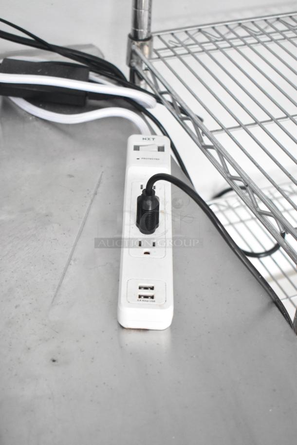 Power strip on stainless steel counter in retail trailer, featuring multiple outlets and USB ports for versatile equipment use.
