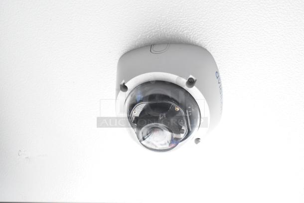 Ceiling-mounted security camera in a white enclosure. Suitable for surveillance in retail or food service environments.
