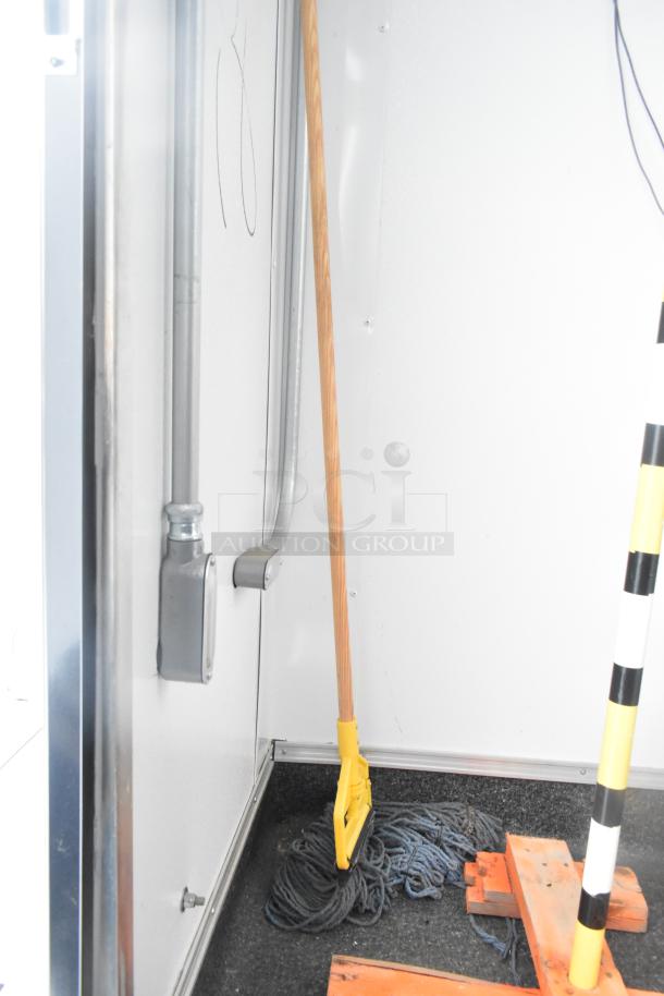 Interior corner of an unbranded retail trailer showing a mop, conduit, and wall fixtures. Clean condition, ready for business.