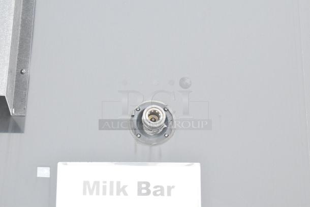 Close-up of an unbranded cold food and beverage trailer showing a "Milk Bar" sign and a hose connection on the exterior.