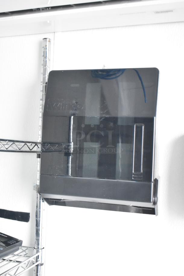 A black wall-mounted paper towel dispenser inside a Nationwide 24' mobile kitchen trailer, with wire shelving nearby.